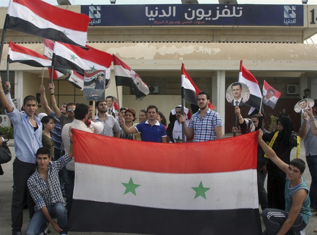 Pro-Syrian regime protesters hold Syrian flags and portraits of Syrian President Bashar Assad, on the airport highway near Damascus, Syria, Sept. 26, 2011.