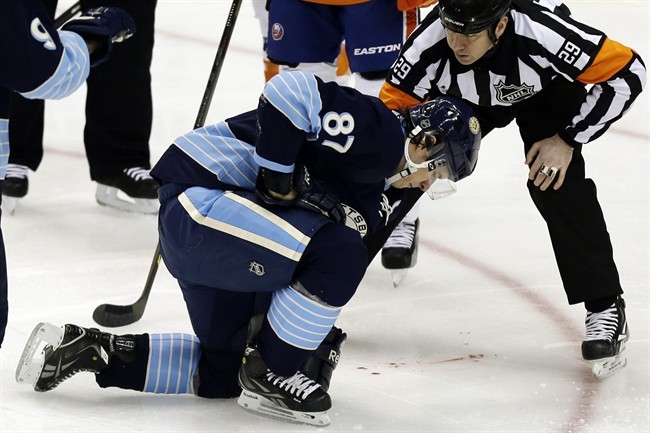 Pittsburgh Penguins center Sidney Crosby (87) is helped by referee Ian Walsh (29) after being hit in the face with a puck during the first period of an NHL hockey game against the New York Islanders in Pittsburgh, Saturday, March 30, 2013. 