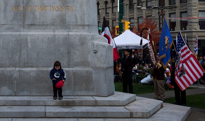 A young First Nations boy stands at the Victory Square Cenotaph as a colour party including veterans hold flags during a National Aboriginal Veterans Day ceremony in Vancouver, on Friday November 8, 2013. The ceremony is held to remember Aboriginal, Metis and Inuit men and women who served in the Canadian Forces. (The Canadian Press/Darryl Dyckber)