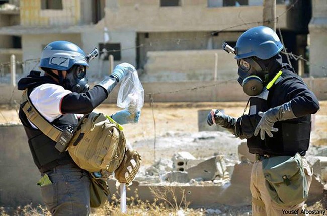  In this Wednesday, Aug. 28, 2013, file photo, a citizen journalism image provided by the United Media Office of Arbeen which has been authenticated based on its contents and other AP reporting, shows members of the United Nations investigation team take samples from sand near a part of a missile that is likely to be a chemical rocket, according to activists, in the Damascus countryside of Ain Terma, Syria. 