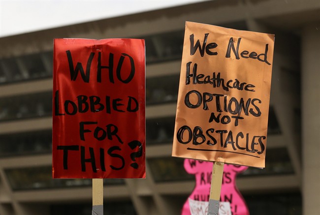 In this July 15, 2013 file photo, two signs that read "Who Lobbied For This?" and "We Need Healthcare Options, Not Obstacles" are held by attendees of a rally in front of Dallas city hall where a group of nearly 200 gathered to protest the approval of sweeping new restrictions on abortion in Texas. A U.S. appeals court on Thursday, Oct. 31, 2013, issued a ruling reinstating most of Texas' tough new abortion restrictions, which means as many as 12 clinics will not be able to perform the procedure starting as soon as Friday. 