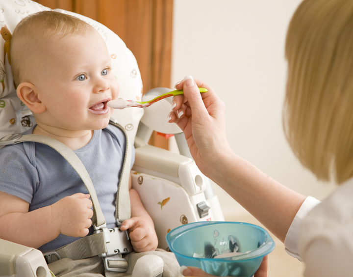 Baby sitting in his highchair with his mother feeding him