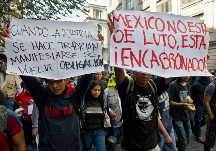 Mexico City:People hold signs reading, “When injustice becomes a tradition, protesting becomes a duty” and “Mexico is not in mourning, it is pissed off,” as they take part in a protest against Mexican President Enrique Pena Nieto, on the first anniversary of his government in Mexico City on Dec. 1, 2013. (Photo credit: Getty Images)