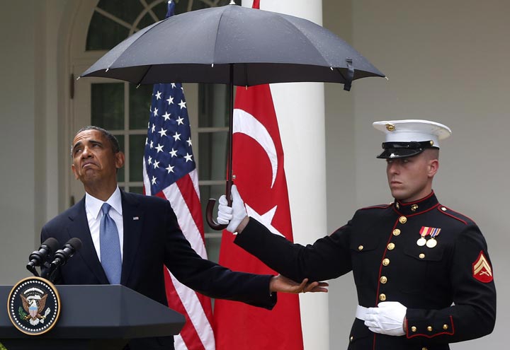 U.S. President Barack Obama looks to see if it is still raining as a Marine holds an umbrella for him during a news conference in the Rose Garden of the White House in Washington. (AP Photo/Charles Dharapak)