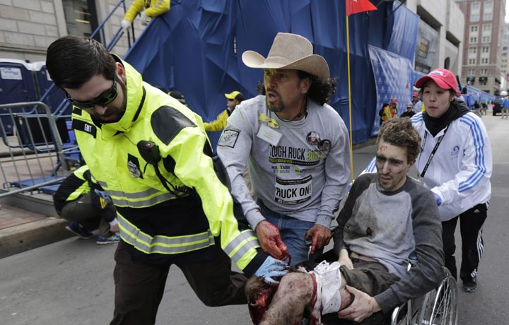 An emergency responder and volunteers push Jeff Bauman in a wheel chair after he was injured in an explosion near the finish line of the Boston Marathon. (AP Photo/Charles Krupa)