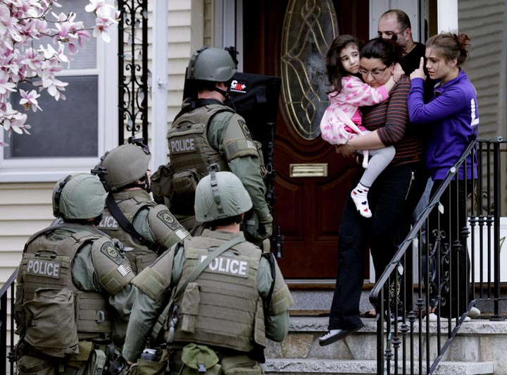 A woman carries a girl from their home as a SWAT team searching for a suspect in the Boston Marathon bombings enters the building in Watertown, Mass. (AP Photo/Charles Krupa, File)