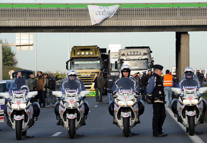 France:French policemen take position as trucks block a section of highway A25 in Englos to protest the “ecotax,” a controversial tax on heavy vehicles, on Dec. 2, 2013. French President Francois Hollande’s government has already been forced to suspend the planned introduction of a new environmental “ecotax” on commercial vehicles carrying cargo of more than 3.5 tonnes after violent protests in Brittany, a predominantly agricultural region in northwestern France. Opponents of the tax, which critics say unfairly penalises remote areas dependent on deliveries by road freight, are demanding it be scrapped altogether. (Photo credit: Getty Images)