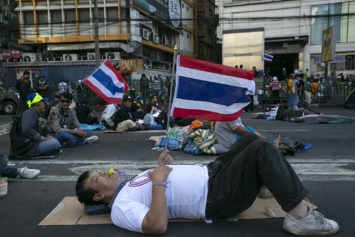 An anti-government protester rests on the street of a major intersection in downtown Bangkok