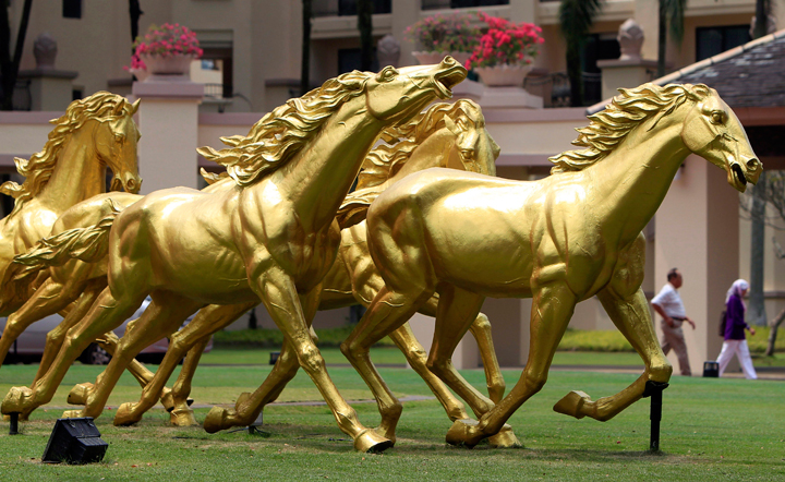 People walk past golden horse statues on display in front of a hotel in Kuala Lumpur, Malaysia, Saturday, Jan. 25, 2014. (Photo credit: Lai Seng Sin/AP Photo)