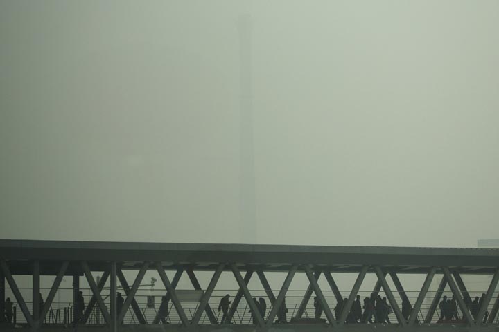 A chimney of a heating plant is obscured by heavy haze as commuters walk through a bridge on a severely polluted day in Beijing Tuesday, Feb. 25, 2014. (AP Photo/Alexander F. Yuan)