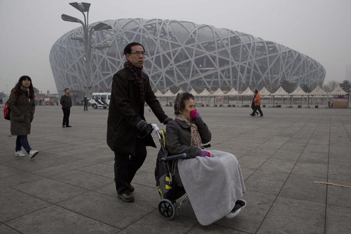 A woman in a wheelchair covers her face as she passes by the iconic bird’s nest National Stadium on a hazy day in Beijing, China, Sunday, Feb. 23, 2014. (AP Photo/Ng Han Guan)