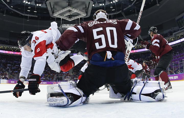 Canada forward Corey Perry trips over Latvia goaltender Kristers Gudlevskis in the first period of a men’s ice hockey game at the 2014 Winter Olympics, Wednesday, Feb. 19, 2014, in Sochi, Russia. (AP Photo/Julio Cortez)