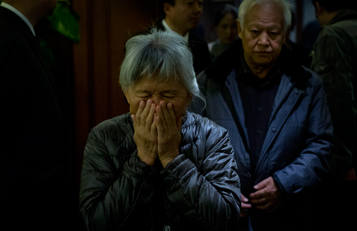 An elderly woman, one of the relatives of Chinese passengers aboard missing Malaysia Airlines Flight MH370, covers her face out of frustration as she leaves the hotel ballroom.