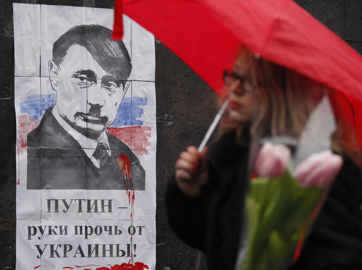 A woman walks in front of poster depicting Russian President Vladimir Putin as Adolf Hitler and signed "Hands off  Ukraine" in Kiev on March 3, 2014.  Yury Kirnichny/AFP/Getty Images.