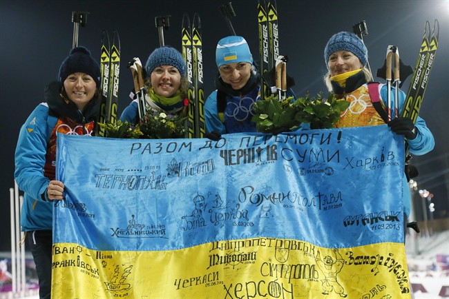 FILE - In this Friday, Feb. 21, 2014, file photo Ukraine's relay team Vita Semerenko, Juliya Dzhyma, Olena Pidhrushna and Valj Semerenko, from left, celebrate with a Ukrainian flag with writings on it after winning the gold during the women's biathlon 4x6k relay, at the 2014 Winter Olympics in Krasnaya Polyana, Russia.