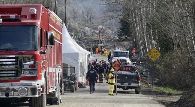 Emergency personnel stage on Highway 530 as work to clear debris from the roadway left behind from a deadly mudslide continues behind, Wednesday, April 2, 2014, in Oso, Wash. 