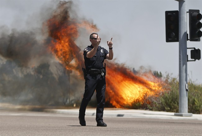 A Carlsbad,Calif. police officer turns traffic away as flames leap behind him Wednesday, May 14, 2014, in Carlsbad, Calif.
