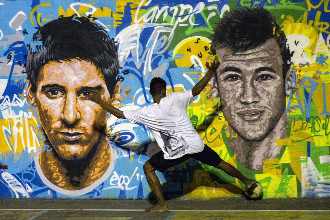 Youngsters play football in front of a mural of Argentine football player Lionel Messi (L) and Brazil's player Neymar da Silva Santos Junior at a field of Tavares Bastos shantytown (favela) in Rio de Janeiro, Brazil on June 8, 2014, just four days ahead of the FIFA World Cup 2014. AFP PHOTO / YASUYOSHI CHIBA (Photo credit should read YASUYOSHI CHIBA/AFP/Getty Images)