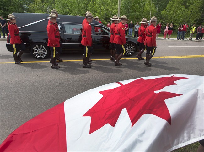 Onlookers wave a Canadian flag during the funeral procession for the three RCMP officers who were killed in the line of duty in Moncton, N.B. on Tuesday, June 10, 2014.