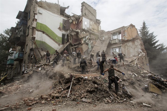 A man walks in a bomb crater near a damaged private house after an airstrike in Snizhne, 100 kms east from the city of Donetsk, eastern Ukraine Tuesday, July 15, 2014. An airstrike demolished an apartment block in eastern Ukraine on Tuesday, killing at least 11 civilians, rescue workers said. 