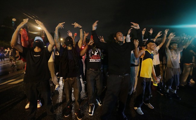 People defy a curfew Sunday, Aug. 17, 2014, before smoke and tear gas was fired to disperse a crowd protesting the shooting of teenager Michael Brown last Saturday in Ferguson, Mo. Brown\’s shooting in the middle of a street following a suspected robbery of a box of cigars from a nearby market has sparked a week of protests, riots and looting in the St. Louis suburb.