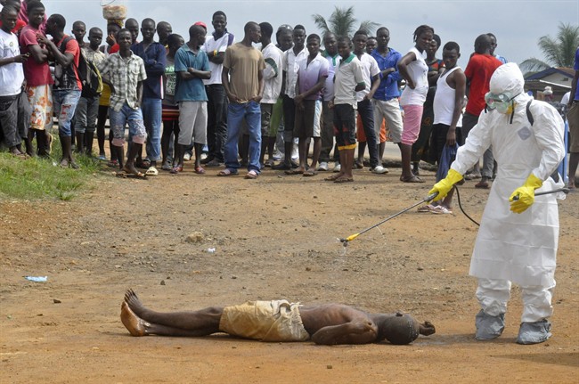 A health worker, right, sprays a man with disinfectant chemicals as he is suspected of dying due to the Ebola virus as people, rear, look on in Monrovia, Liberia, Thursday, Sept. 4, 2014. 