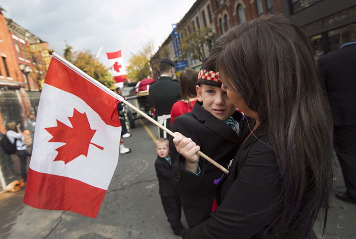 Marcus Cirillo, 5, the son of Nathan Cirillo, accompanied by his aunt, Natasha Cirillo, holds a flag during a short pause as the body of Nathan Cirillo is escorted through the streets toward his funeral service in Hamilton, Ont., on Tuesday, October 28, 2014. THE CANADIAN PRESS/Peter Power