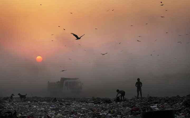 A thick blanket of smoke is seen against the setting sun as young ragpickers search for reusable material at a garbage dump in New Delhi, India, Friday, Oct. 17, 2014. The WHO says that 1.7 million children die every year due to polluted environments.