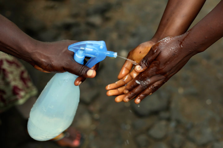 In this photo taken on Thursday Oct. 2, 2014, Promise Cooper, 16, has her hands cleaned with a chlorine solution by Kanyean Molton Farley, a community activist who visits Promise and her two brothers, Emmanuel Junior, 11, and Benson, 15, on a daily basis at their St. Paul Bridge home in Monrovia, Liberia. The Cooper children are now orphans, having lost their mother Princess in July, and their father Emmanuel in August. Their 5-month-old baby brother Success also succumbed to the virus in August.