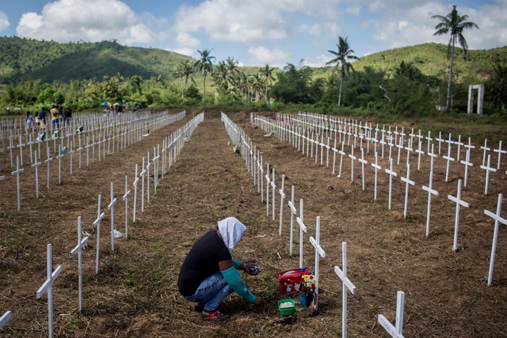 A woman sits at the cross of a loved one at the mass grave on the grounds of the Holy Cross Memorial Garden on November 8, 2014 in Tacloban, Leyte, Philippines.