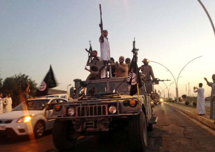 In this photo taken Monday, June 23, fighters from the Islamic State group parade in a commandeered Iraqi security forces armored vehicle down a main road at the northern city of Mosul, Iraq. 