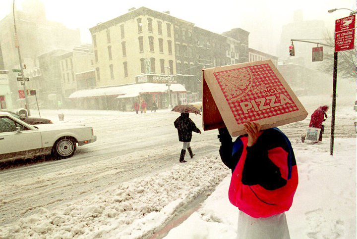 A pizza delivery man shields himself from the blizzard conditions pounding New York City and most of the east coast of the U.S. as he waits to cross second Avenue 13 March 1993.