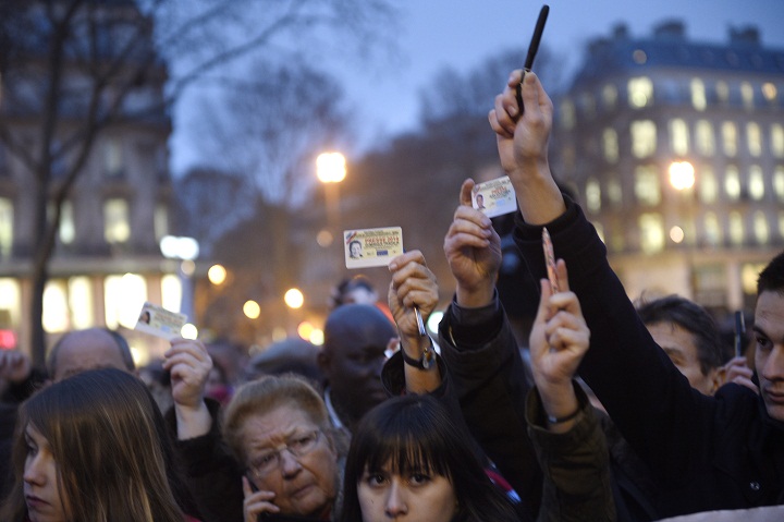 Journalists raise their press cards as others hold up pens during a gathering at the Place de la Republique (Republic square) in Paris, on January 7, 2015.