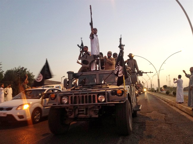 In this photo taken Monday, June 23, 2014, fighters from the Islamic State group parade in a commandeered Iraqi security forces armored vehicle down a main road in Mosul, Iraq.