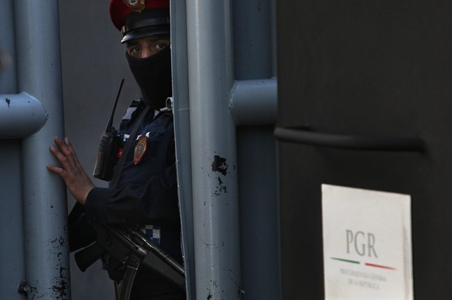 A masked federal police officer stands guard as part of increased security at the organized-crime division of Mexico's Attorney General Office where high profile detainees are sometimes held and shown to the press in Mexico City, Friday, Feb. 27, 2015. 