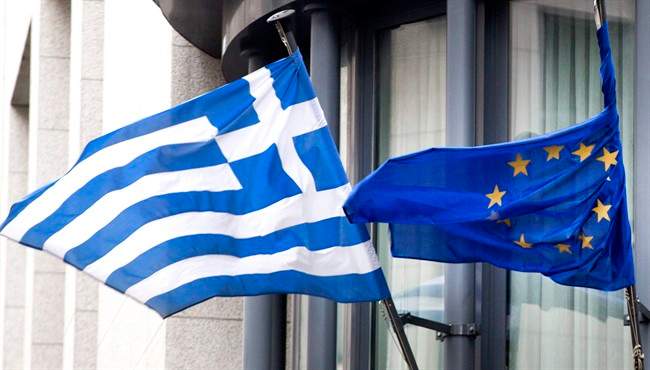 The Greek, left, and EU flag flap in the wind outside the Greek embassy in Brussels on Friday, Feb. 20, 2015.