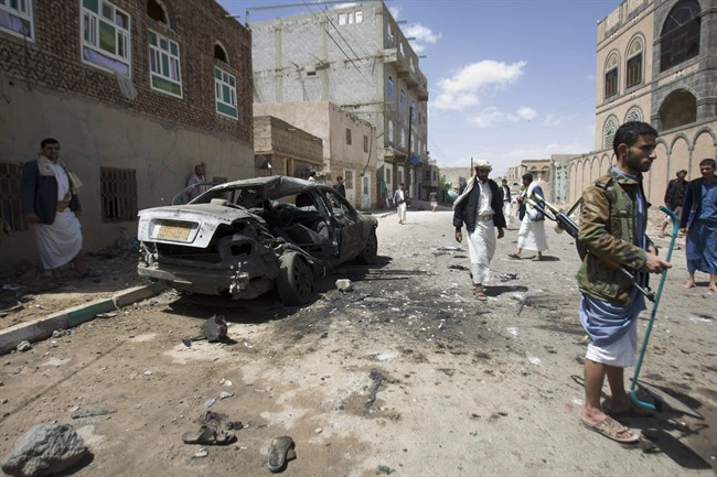 Shiite rebels, known as Houthis, stand near a damaged car after a bomb attack in Sanaa, Yemen, Friday, March 20, 2015. 