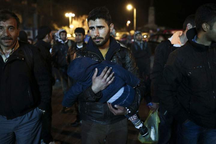 A migrant holds his child in the port of Lesvos island as he waits to board a ship to Athens on April 17, 2015.