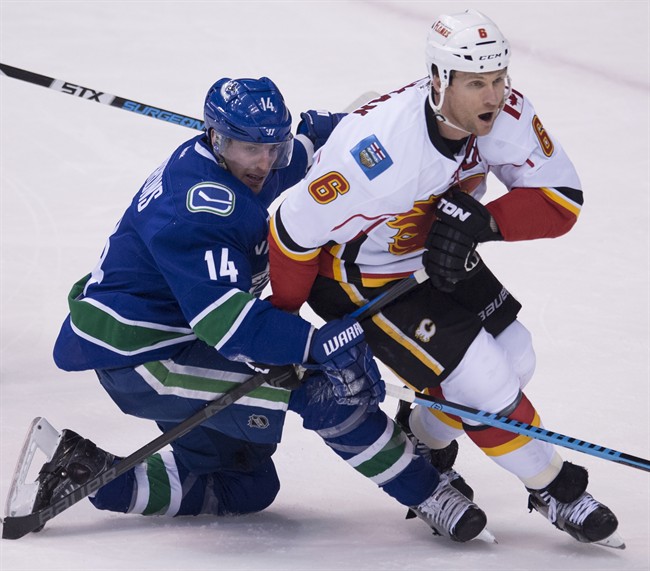 Vancouver Canucks left wing Alex Burrows (14) fights for control of the puck with Calgary Flames defenseman Dennis Wideman (6) during the second period of NHL playoff action in Vancouver, B.C. Wednesday, April 15, 2015. Burrows was taken to hospital Tuesday after suffering an unspecified injury at the team's morning skate.THE CANADIAN PRESS/Jonathan Hayward.