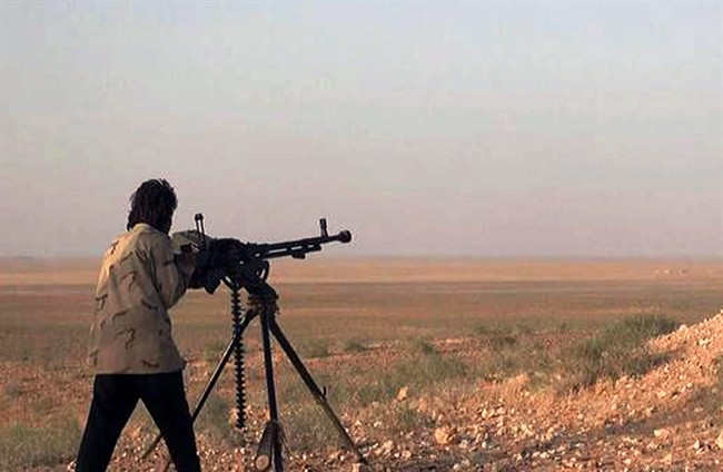 In this picture released on Wednesday, May 20, 2015 by the website of Islamic State militants, an Islamic State fighter aims his weapon during a battle against the Syrian government forces on a road between Homs and Palmyra, Syria. 