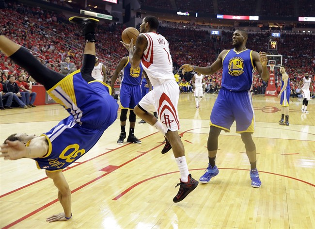 Golden State Warriors guard Stephen Curry (30) topples over Houston Rockets forward Trevor Ariza (1) during the first half in Game 4 of the Western Conference finals of the NBA basketball playoffs as center Festus Ezeli (31) looks on, Monday, May 25, 2015, in Houston. 