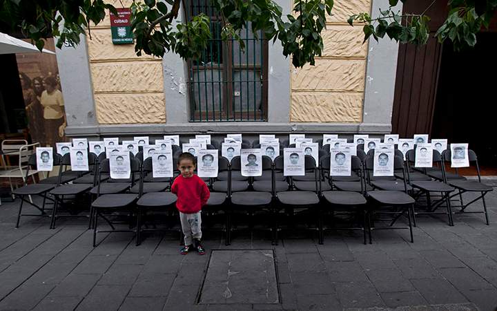A child stands before a memorial made up of empty chairs bearing images of the 43 missing students, to mark the nine-month anniversary of their disappearance, in Mexico City, Saturday, June 27, 2015.