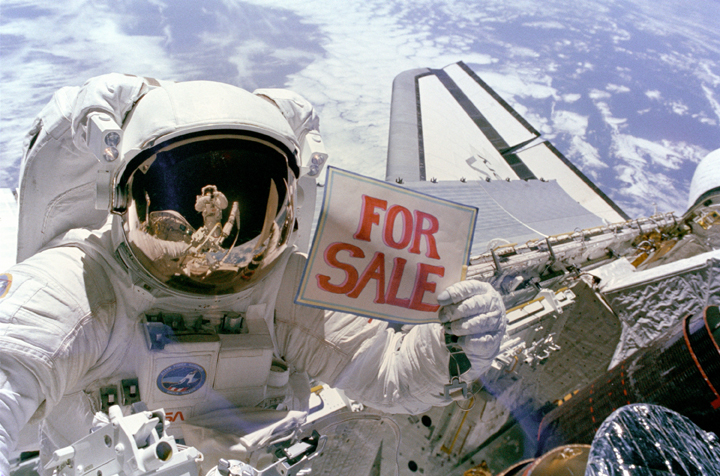 Astronaut Dale Gardner holds up a “For Sale” sign referring to two satellites that were retrieved during a spacewalk on Nov. 14, 1984.