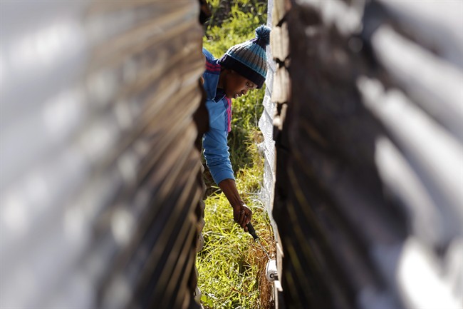 A child paints a shack with white fire retardant paint as a contribution to International Nelson Mandela day celebrating former South African president Mandela's birthday in the township of Nomzamo, South Africa, Saturday, July 18, 2015. 