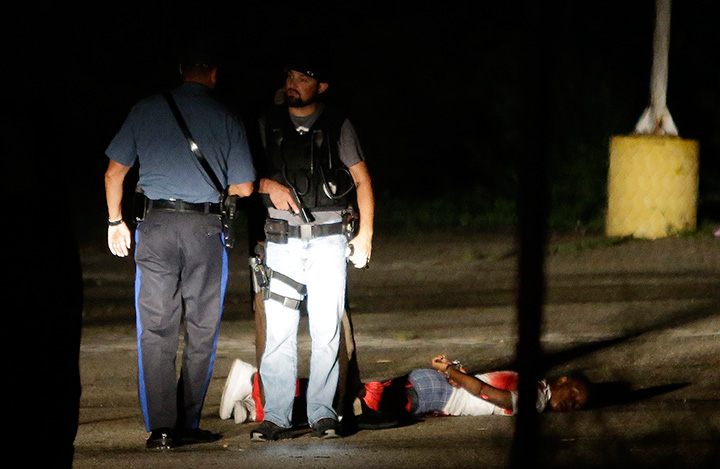Police stand near a suspect in a parking lot after gunfire erupted during a protest on the anniversary of the death of Michael Brown, Sunday, Aug. 9, 2015, in Ferguson, Mo.