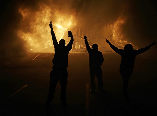 In this Nov. 25, 2014, file photo, people watch as stores burn in Ferguson, Mo., after a grand jury decided not to indict Ferguson police Officer Darren Wilson in the death of Michael Brown, the unarmed, black 18-year-old whose fatal shooting sparked sometimes violent protests. 