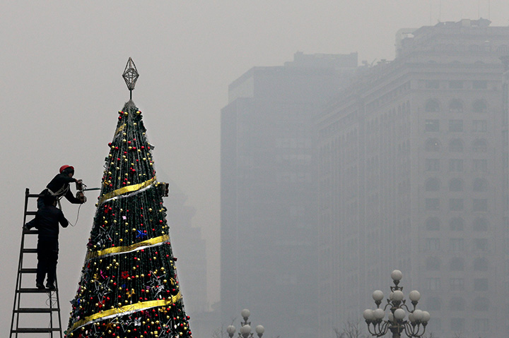 Workers install a Christmas tree on display outside a shopping mall during a day of heavy pollution in Beijing, Tuesday, Dec. 8, 2015.