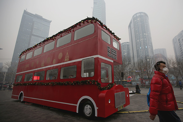 A man wearing a mask passes a double-decker bus model during a day of heavy pollution on December 8, 2015 in Beijing, China.