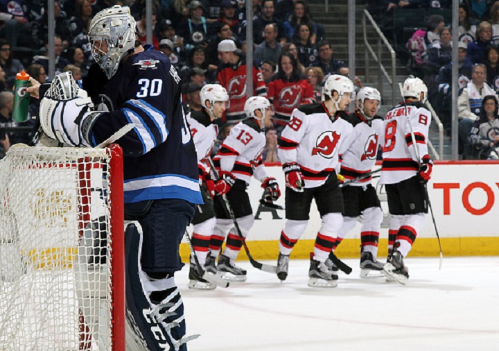 Winnipeg Jets goalie Connor Hellebuyck turns away as the New Jersey Devils celebrate a first period goal.