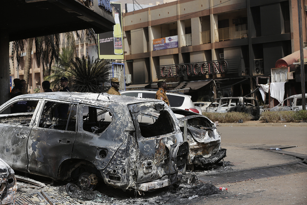 Soldiers walk past burnt cars outside the Cappuccino cafe that was attacked Saturday by suspected militants in Ouagadougou, Burkina Faso, Sunday, Jan. 17, 2016.